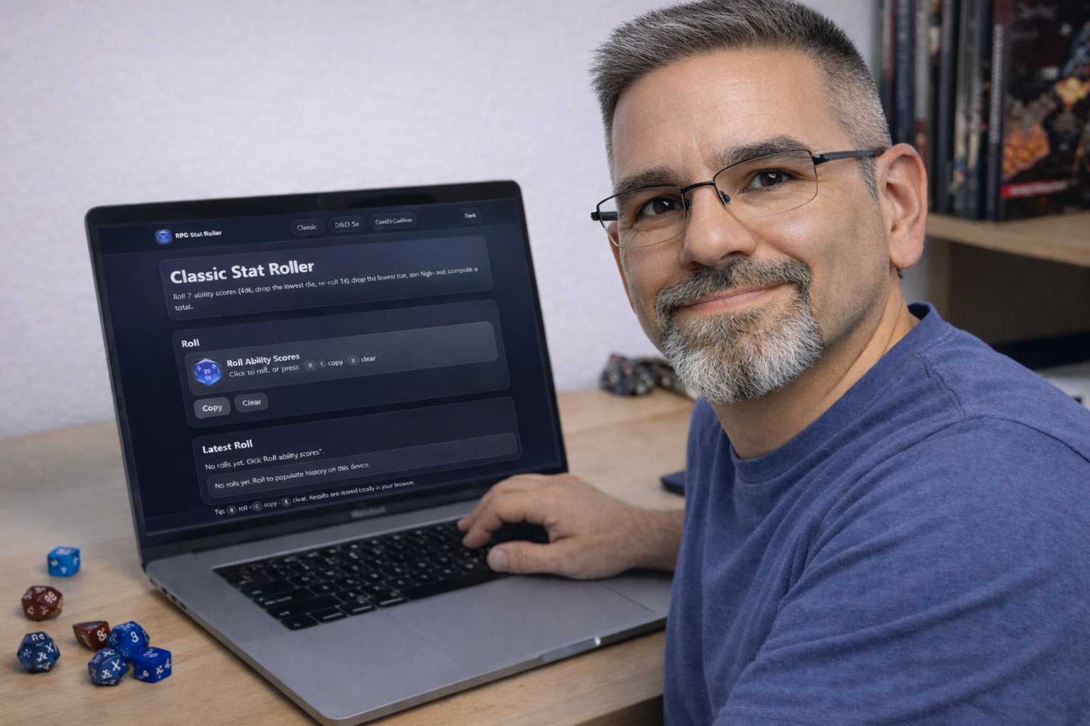 Frank Jamison sits at a wooden desk wearing a blue shirt, looking at the camera with a natural, relaxed expression while using his laptop. The screen displays the RPG Stat Roller web application in dark mode, and several blue and red polyhedral dice are arranged on the desk beside the computer, with RPG books visible on a shelf in the background.